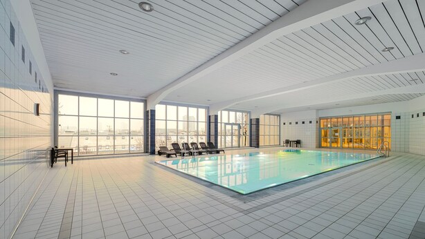 Ein moderner, überdachter Pool mit Panoramafenstern, Fliesenboden und Blick auf die Stadt.
