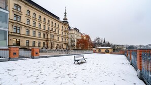 Ein verschneiter Innenhof mit einer Bank, einem Zaun und Gebäuden im Hintergrund.