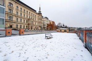 Un patio cubierto de nieve con una banca, una valla y edificios al fondo.