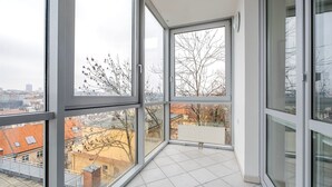 Eine hohe Wohnung mit großen Fenstern, Fliesenboden und Blick auf die Stadtlandschaft.