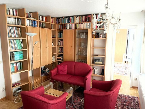 A living room with a red sofa, a glass coffee table, and a bookshelf filled with books. - Hekmat Apartments Nordseeblick Schobüll (Husum)