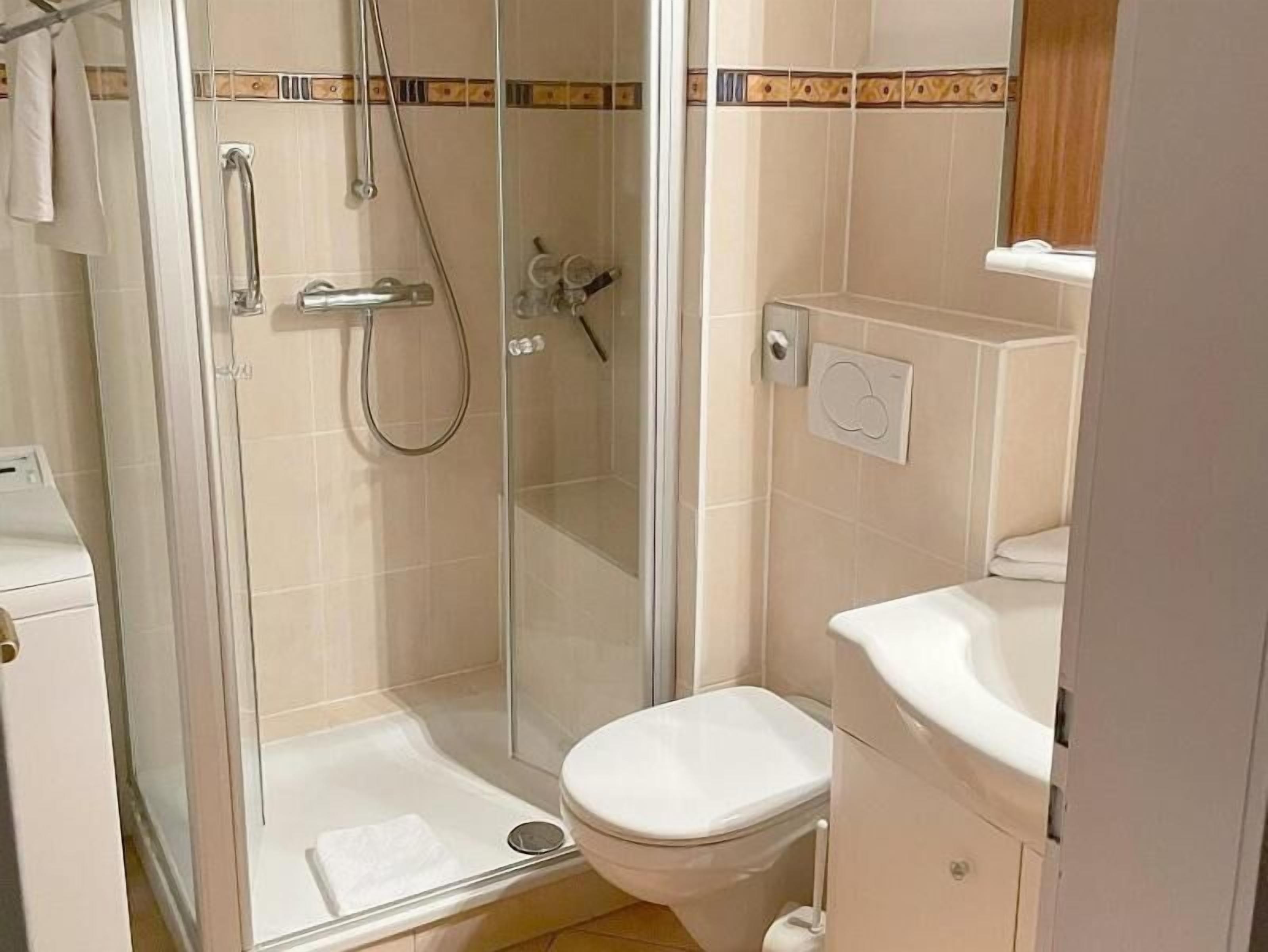 A small bathroom with a glass shower enclosure, a toilet, and a sink.