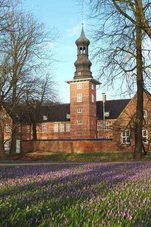 A historic building with a prominent tower and a field of purple flowers in the foreground. - Hekmat Apartments Nordseeblick Schobüll (Husum)