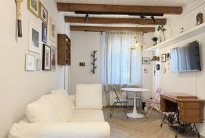 Un soggiorno con un divano bianco, un tavolino rotondo, una scrivania in legno e una televisione appesa al muro.
