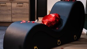 A modern lounge chair with a black leather seat and red rose petals, placed on a wooden floor.