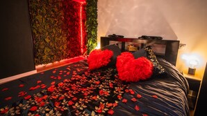 A bedroom with a bed, pillows, a bedside table, and a wall with a red light.