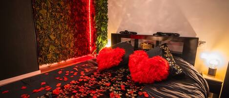 A bedroom with a bed, pillows, a bedside table, and a wall with a red light.