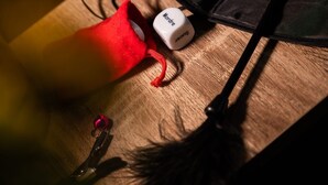A wooden surface with a black hat, a red object, a white dice, and a feather.
