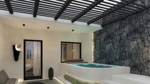A modern spa area with a hot tub, a seating area with a sofa and a table, and a stone wall. - Mamay Hotel (Santorini)