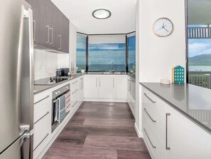 Eine moderne Küche mit Meerblick, weißen Schränken, Edelstahlgeräten und einer Uhr an der Wand.