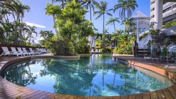 A pool surrounded by palm trees and lounge chairs, with a building in the background. - Luxury Waterfront: Spectacular Oasis in the City (Cairns North)