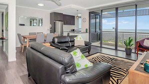 A modern living room with a leather sofa, a dining table, and a view of the ocean through large windows. - Luxury Waterfront: Spectacular Oasis in the City (Cairns North)