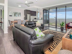 Ein modernes Wohnzimmer mit Ledersofa, einem Esstisch und Blick auf das Meer durch große Fenster.
