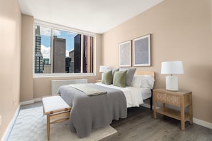 Un dormitorio con un ventanal grande, una cama con almohadas, una mesita de noche con lámpara y una obra de arte en la pared.