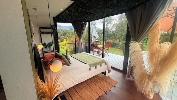 A bedroom with a large bed, a view of the outdoors, and a balcony with a chair.