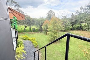 Une vue depuis un balcon donnant sur un espace verdoyant, avec des arbres et un chemin de gravier.