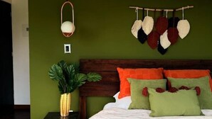 A bedroom with a wooden headboard, a hanging light fixture, a wall-mounted plant, and a wall art piece.