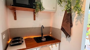 A compact kitchenette with a microwave, stove, sink, and a small trash bin.