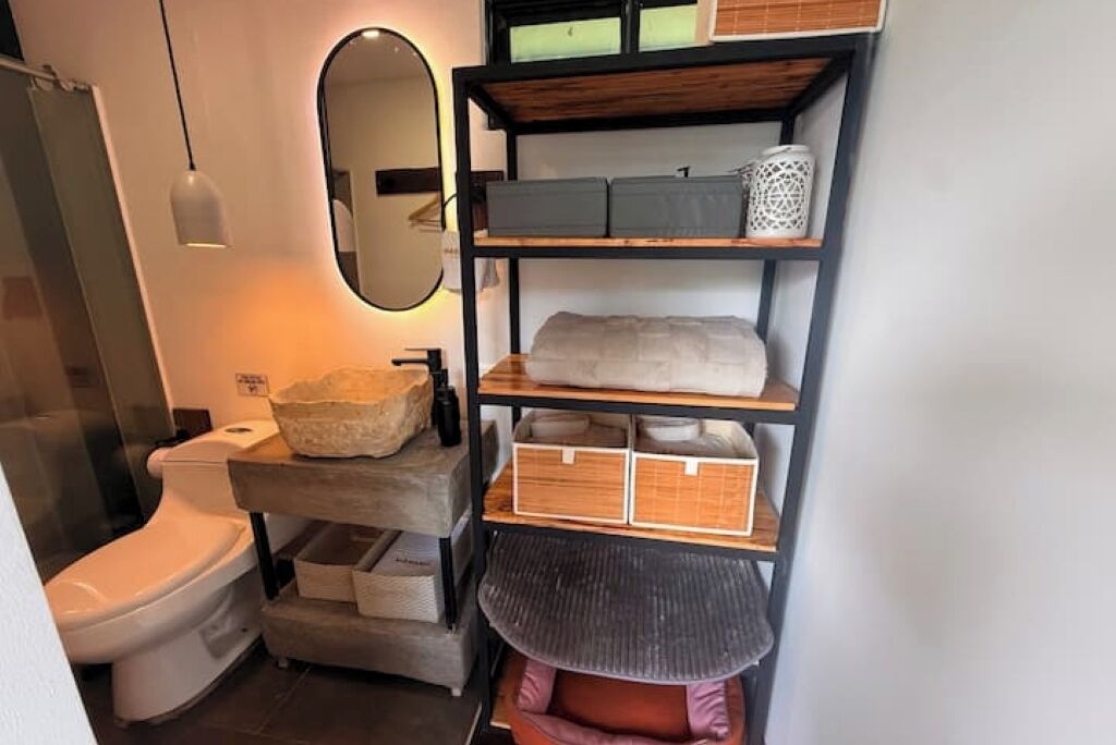Une petite salle de bain comprenant des toilettes, une étagère avec des boîtes de rangement et un miroir.
