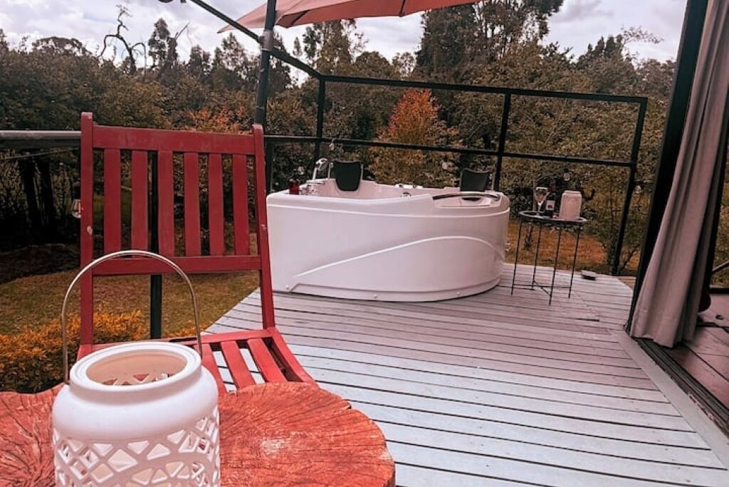En terrass med en röd stol, ett vitt bubbelbad och ett litet bord med flaskor.