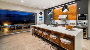 Una cocina moderna con una isla grande, taburetes de bar y vistas al atardecer.