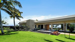 Una casa moderna con césped cuidado, palmeras y vista despejada al océano.
