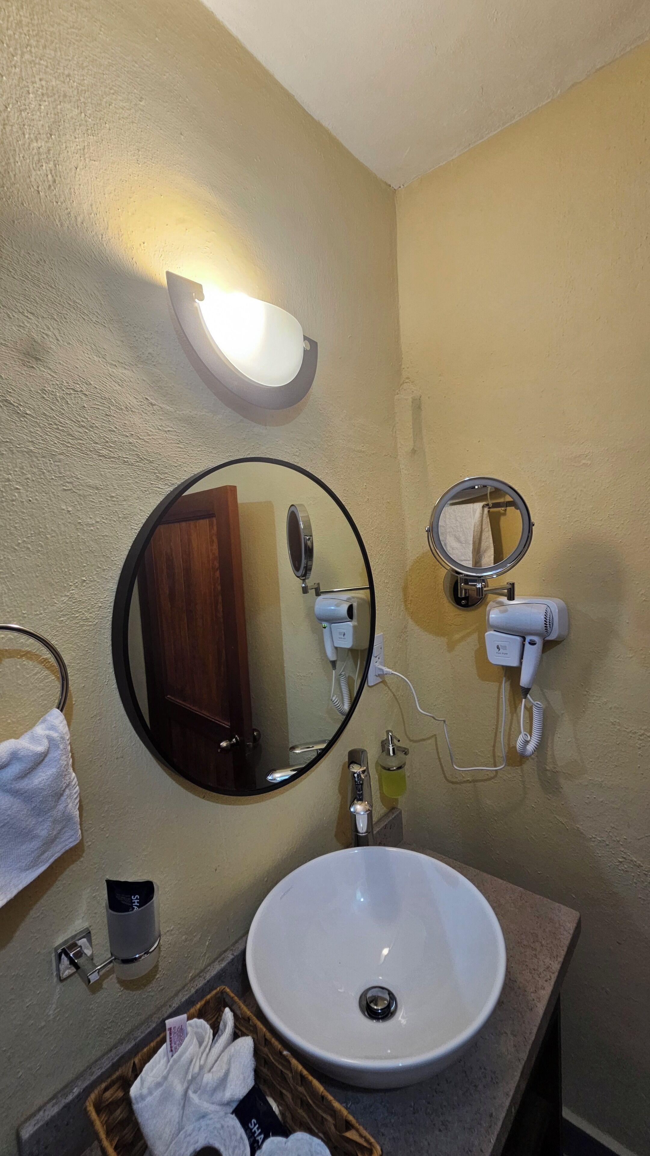 Une salle de bain avec un miroir rond, un lavabo, un porte-serviettes et un sèche-cheveux.