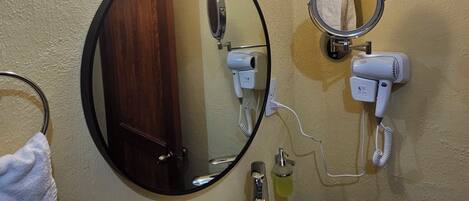 Une salle de bain avec un miroir rond, un lavabo, un porte-serviettes et un sèche-cheveux.