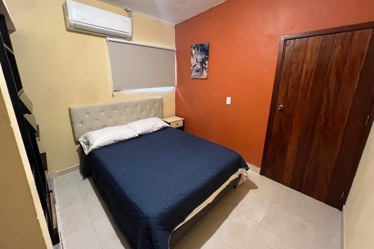 A bedroom with a bed, a nightstand, a wooden door, and an air conditioning unit.