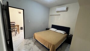 A bedroom with a bed, a nightstand, a wall-mounted air conditioner, and a door leading to a dining area. - Suites el Ángel (Tuxtla Gutiérrez)