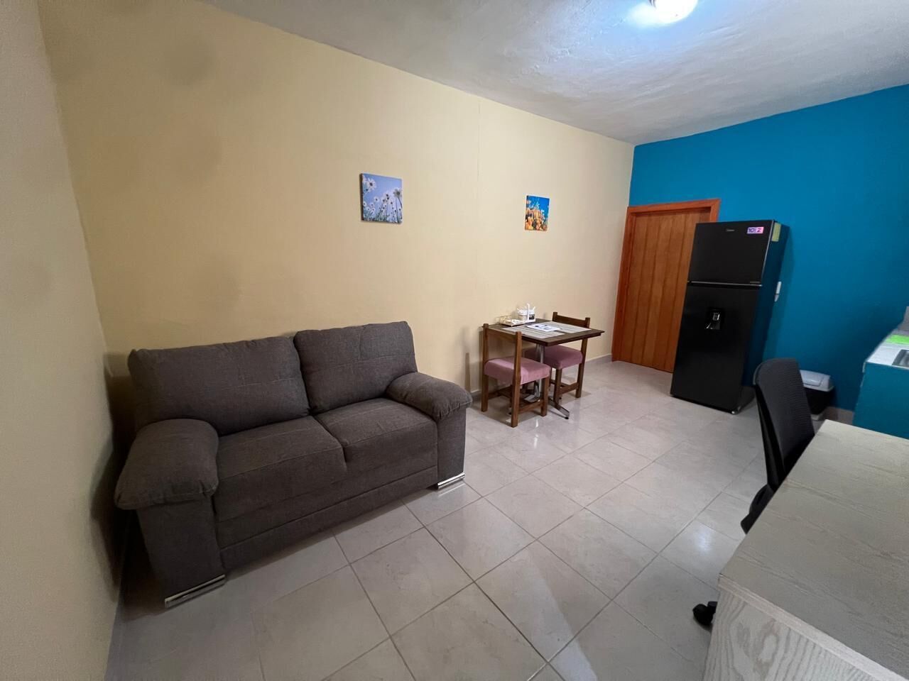 A living room with a sofa, a dining table with chairs, and a refrigerator.