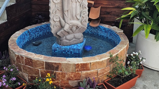 A stone statue in a circular fountain with a wooden backdrop and a staircase. - Suites el Ángel (Tuxtla Gutiérrez)