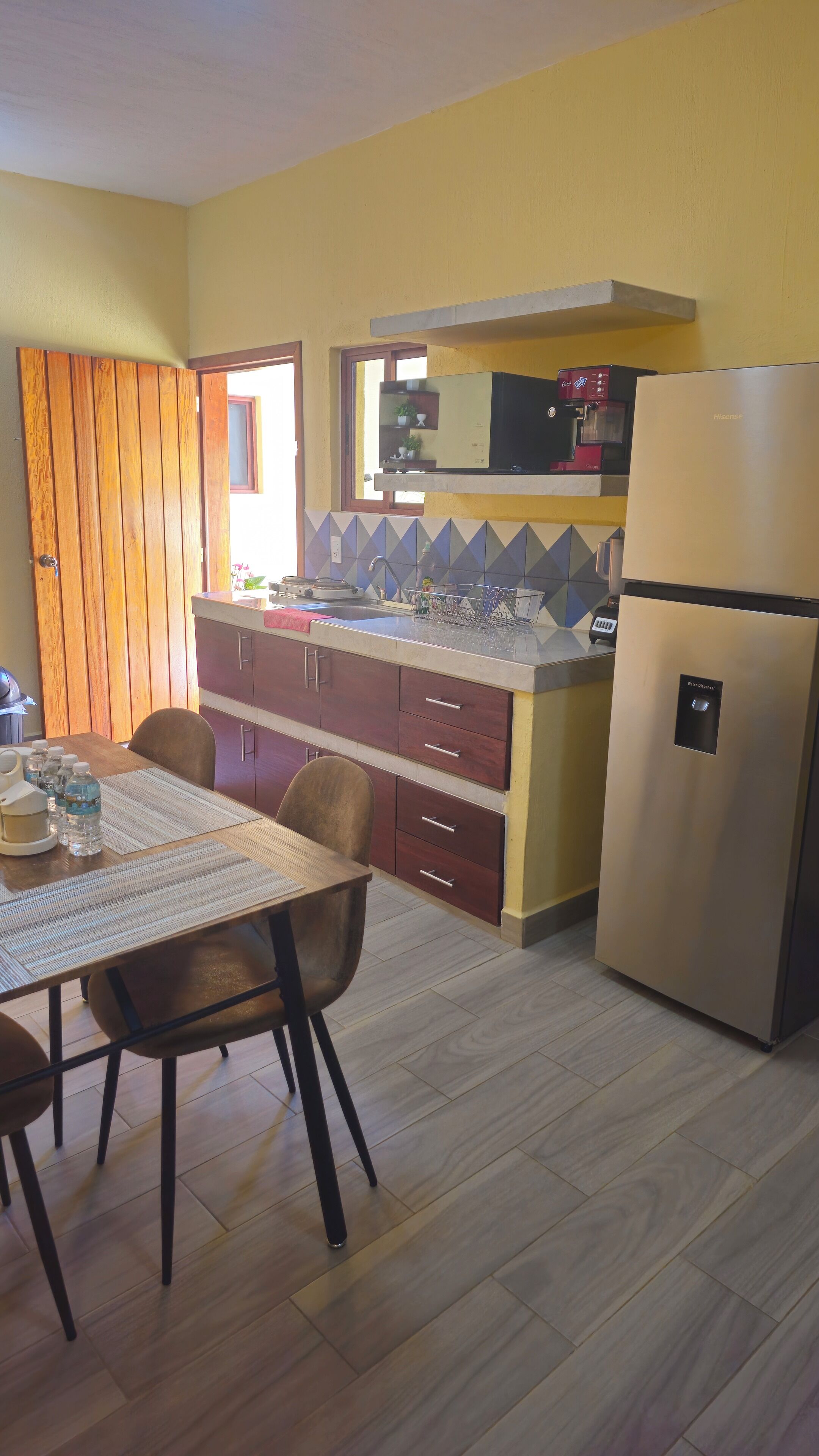 Cocina compacta con comedor, que incluye una puerta de madera, un refrigerador de acero inoxidable y salpicadero de azulejos.