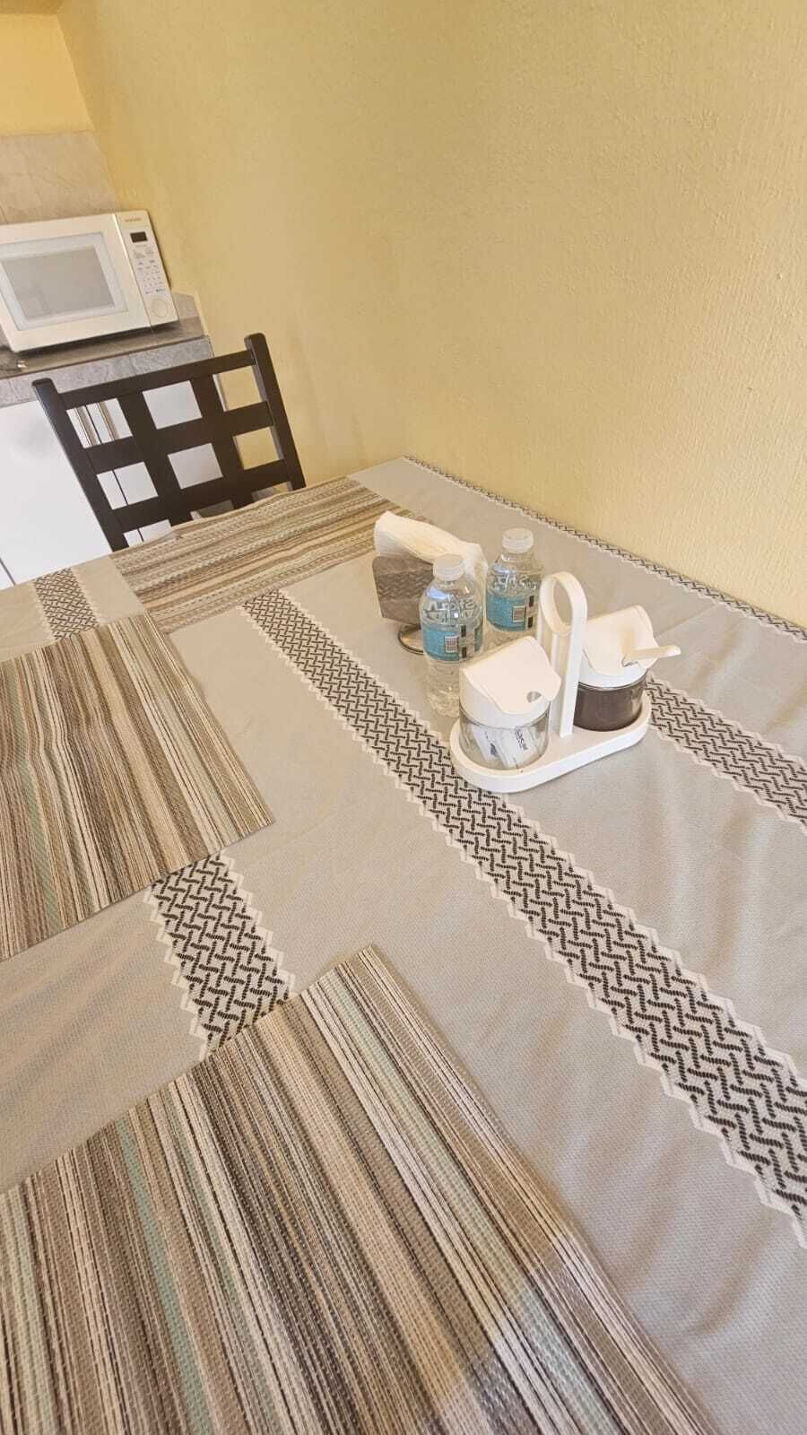 A dining table with a patterned tablecloth, a microwave, water bottles, a white pitcher, and a white cup.