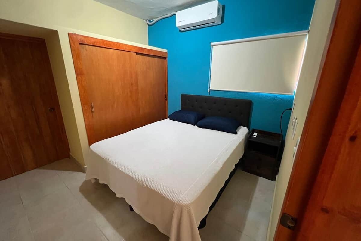 A bedroom with a bed, a wardrobe, a wall-mounted air conditioner, and a whiteboard.