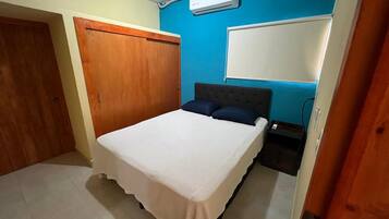Un dormitorio con cama, armario, aire acondicionado instalado en la pared y una pizarra.