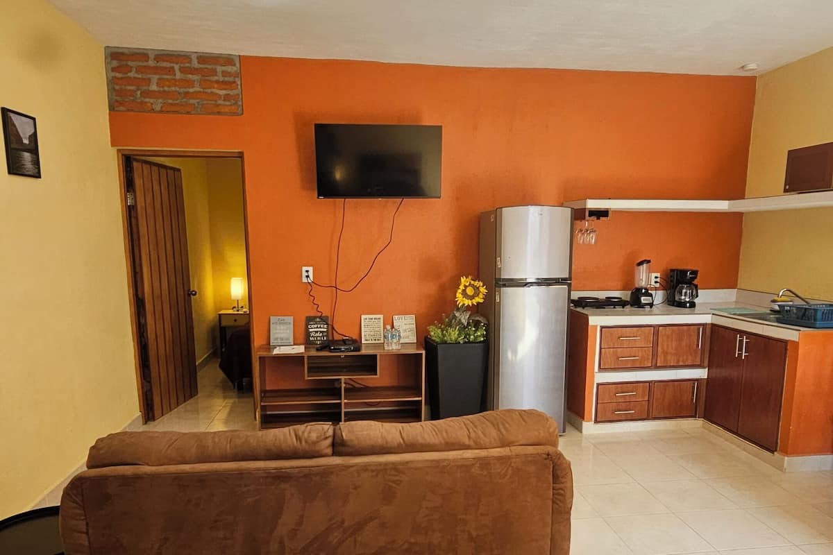 A compact living space with a kitchenette, a sofa, and a flat-screen TV mounted on the wall.