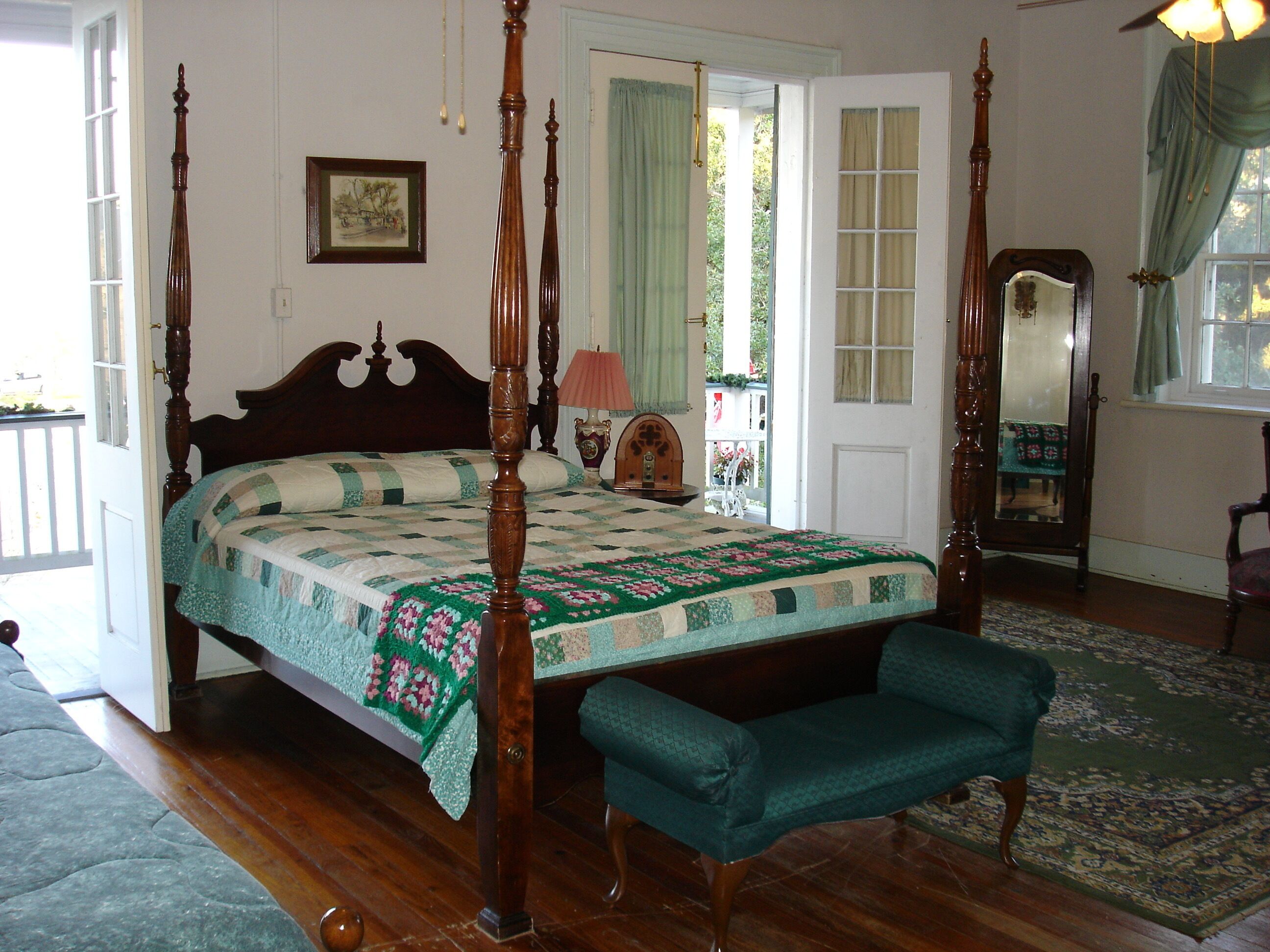 A traditional four-poster bed with a quilt, a bench, and a wooden floor.