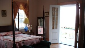 Ein Schlafzimmer mit einem Himmelbett, einem Nachttisch mit Lampe, einer Bank und einer Tür, die auf einen Balkon führt.