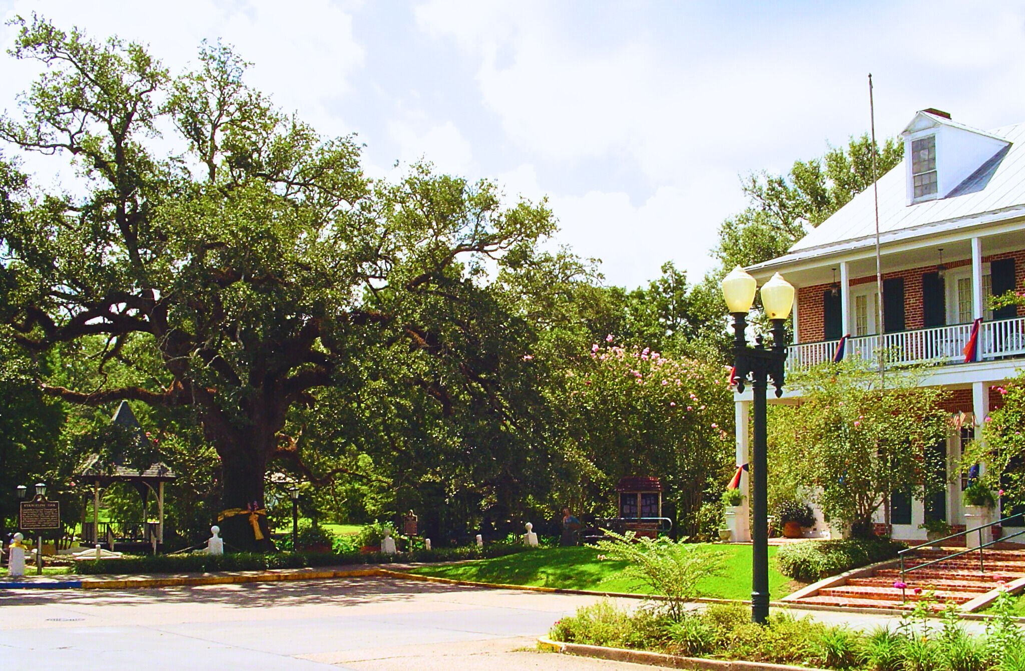 A historic building with a white facade and a balcony, surrounded by lush greenery and a well-maintained lawn.