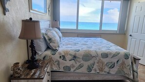 Et soveværelse med seng, ventilator, vindue med havudsigt og lampe på et natbord.