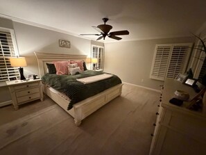 Et soveværelse med seng, natborde, ventilator og kommode.