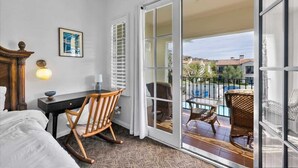 A hotel room with a bed, a desk, a rocking chair, a dining table with chairs, and a balcony with a pool. - Poolside Greens B | Studio Legacy Villa (La Quinta)