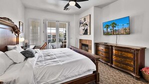 A bedroom with a bed, a ceiling fan, a fireplace, a dresser, and a painting on the wall. - Poolside Greens B | Studio Legacy Villa (La Quinta)