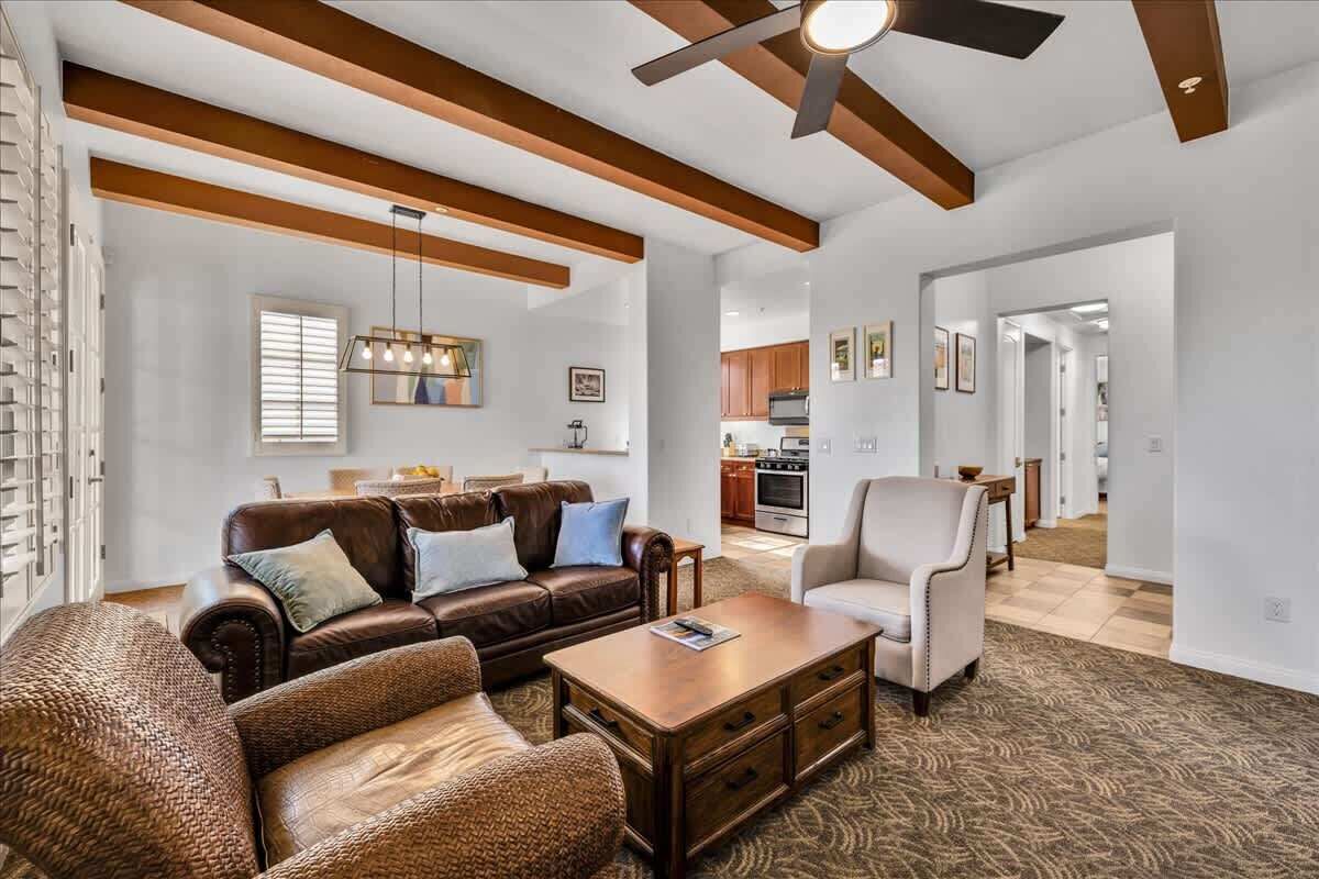 A spacious living room with a brown leather sofa, a wooden coffee table, and a ceiling fan.