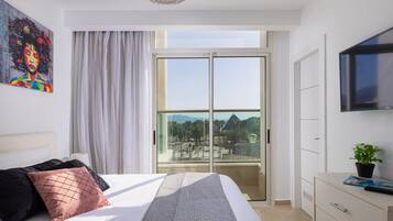 A modern bedroom with a large bed, a sliding glass door to a balcony, a mounted TV, and a painting on the wall.