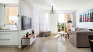 A modern living room with a flat-screen TV, a sofa, a dining table, and a balcony with a view. - Mamad Bright Eilat escape with balcony and pool (Eilat)
