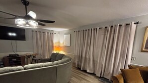 A living room with a sectional sofa, a brown couch, a ceiling fan, a TV, and a lamp.