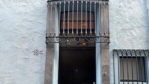 Ein Gebäudeeingang mit einem Metallgitter, einem kleinen, vergitterten Fenster und einer Tür.