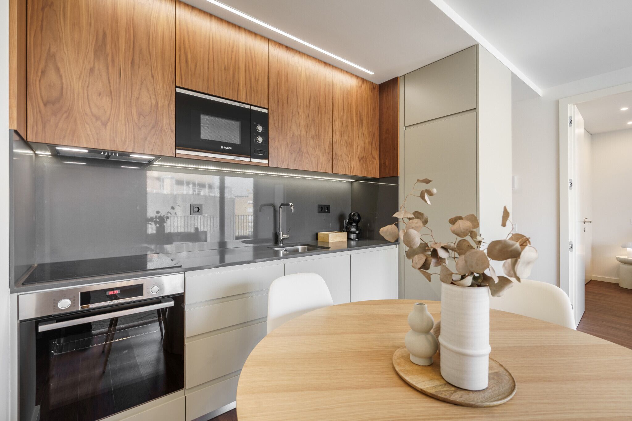 Une cuisine moderne avec des meubles en bois, des appareils en acier inoxydable et un coin repas comprenant une table en bois et un vase.
